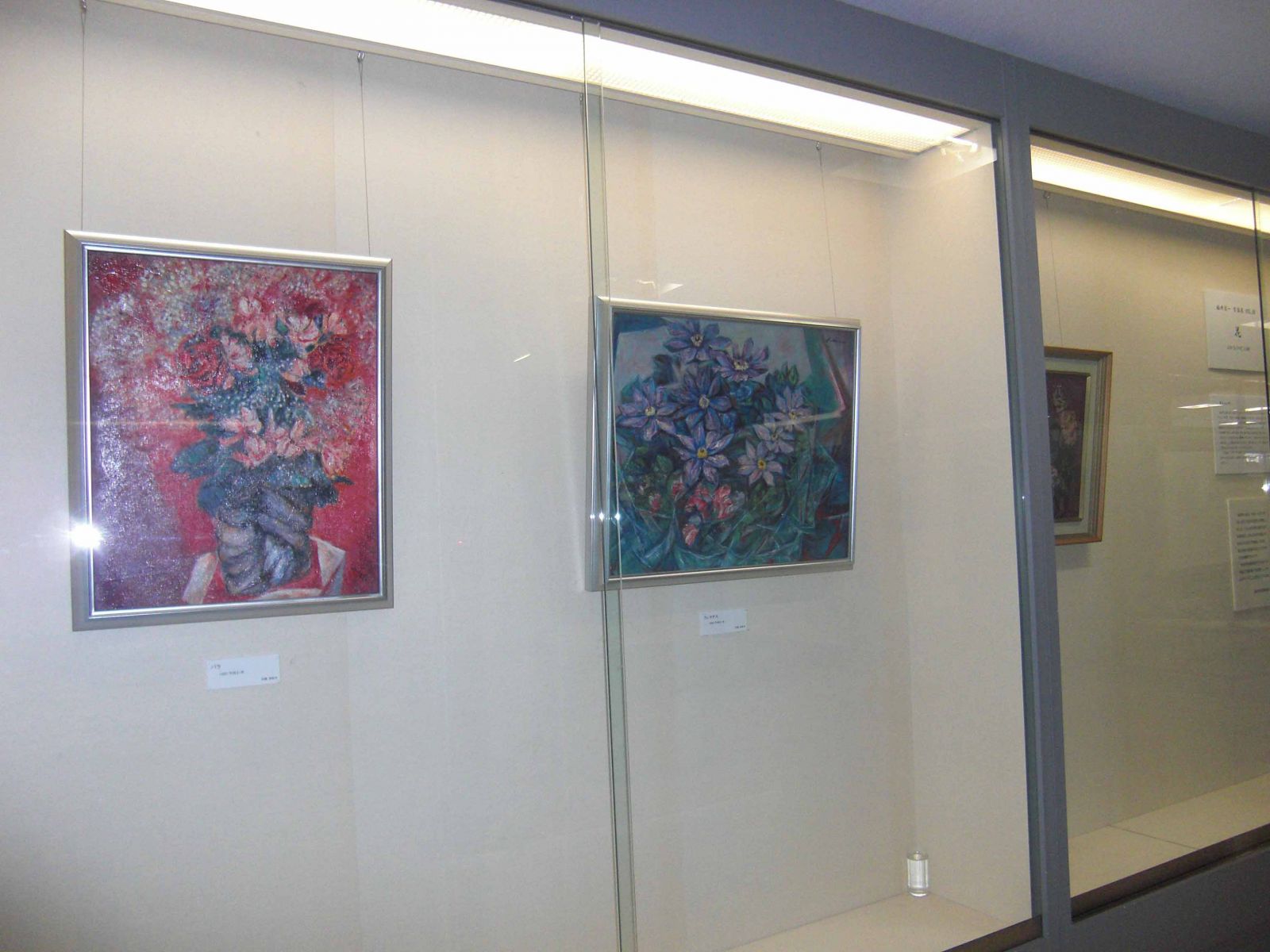 3枚の赤や紫色の花が描かれた絵画が展示された展覧会の写真