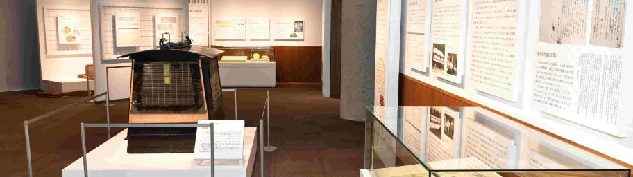 写真や説明文が書かれたパネルが壁に展示され、様々な資料がガラスケースや台に展示されている2階の展示室の写真