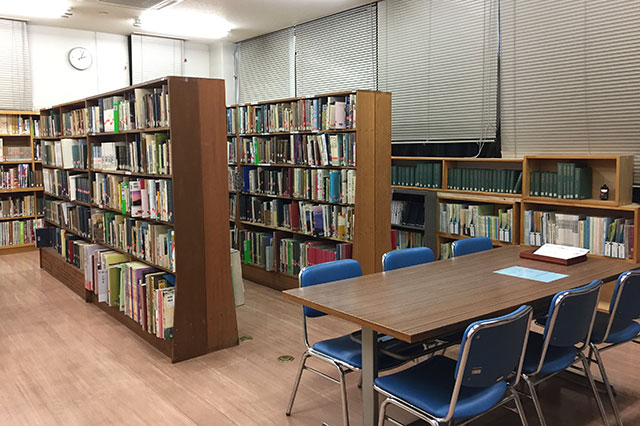 奥に並列する本棚と手前に机・水色の椅子が置かれている郷土資料室の写真