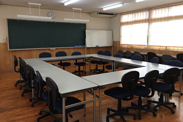 前方に黒板とホワイトボードがあり、ロの字型に設置された長机に椅子が置かれている会議室の写真