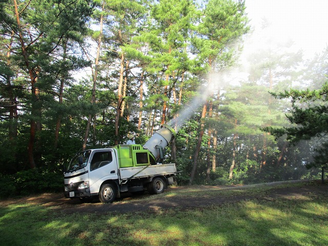 トラックの荷台から薬剤を高圧噴霧器で地上散布している様子の写真