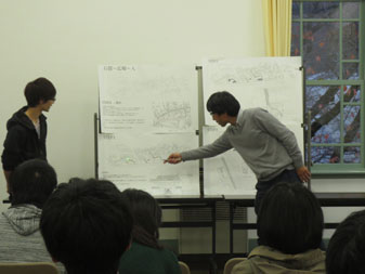 教室の前方に設置されたホワイトボードに資料が貼られ、指を指しながら説明している教師と授業を聞いている生徒達の写真