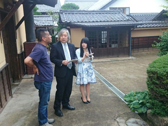 和風造りの建物に囲まれた敷地内で、塩屋醸造の男性と教員の男性が話をし、傍に立ってメモをとっている女生徒の写真