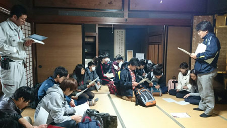 畳が敷かれた和室に立って資料を見ながら話をしている男性と、資料を見ながら座って話を聞いている生徒達の写真