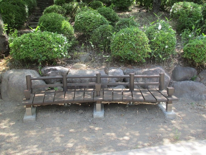 後方には多くの植木が並んでいる場所に、木製のベンチの作品が設置されている写真
