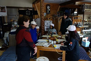 店内でメモを取りながら女性の話を聞いている子どもたちの写真