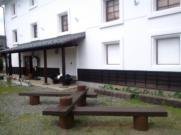 白壁の建物の横に設置された木製のベンチの作品の写真