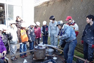 4名の作業服を着た男性と作業を見学する子どもたちの写真