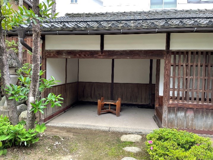 瓦屋根の建物入り口に、組み合わせて作られたベンチの作品が設置されている様子を庭から撮影した写真