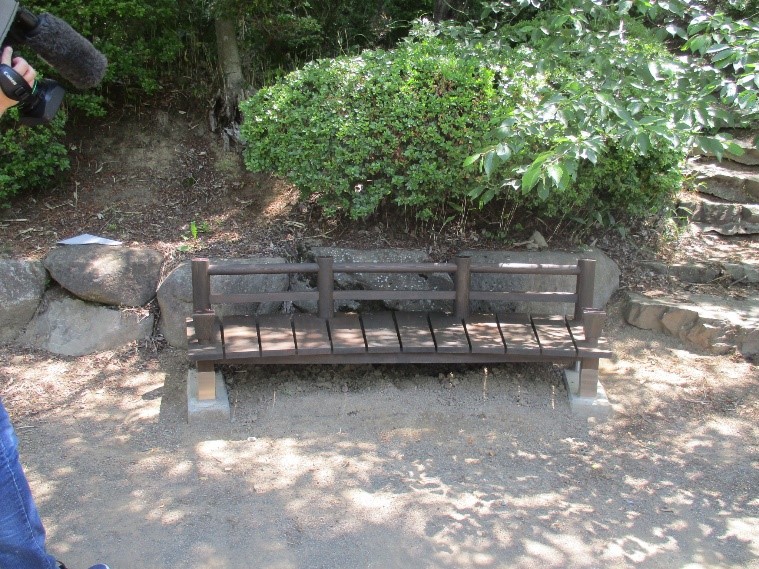 階段の横に設置され、自然の中に溶け込んでいる木製ベンチの作品の写真