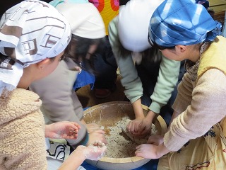 4名でそば粉が入った木製のこね鉢を囲みこねる学生たちの写真