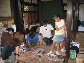 古民家の床や柱に紙を乗せ、色鉛筆でこすって模様を出す学生たちの写真