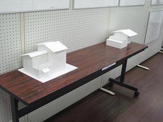 長机に置かれて展示された2つの白い住宅模型の写真