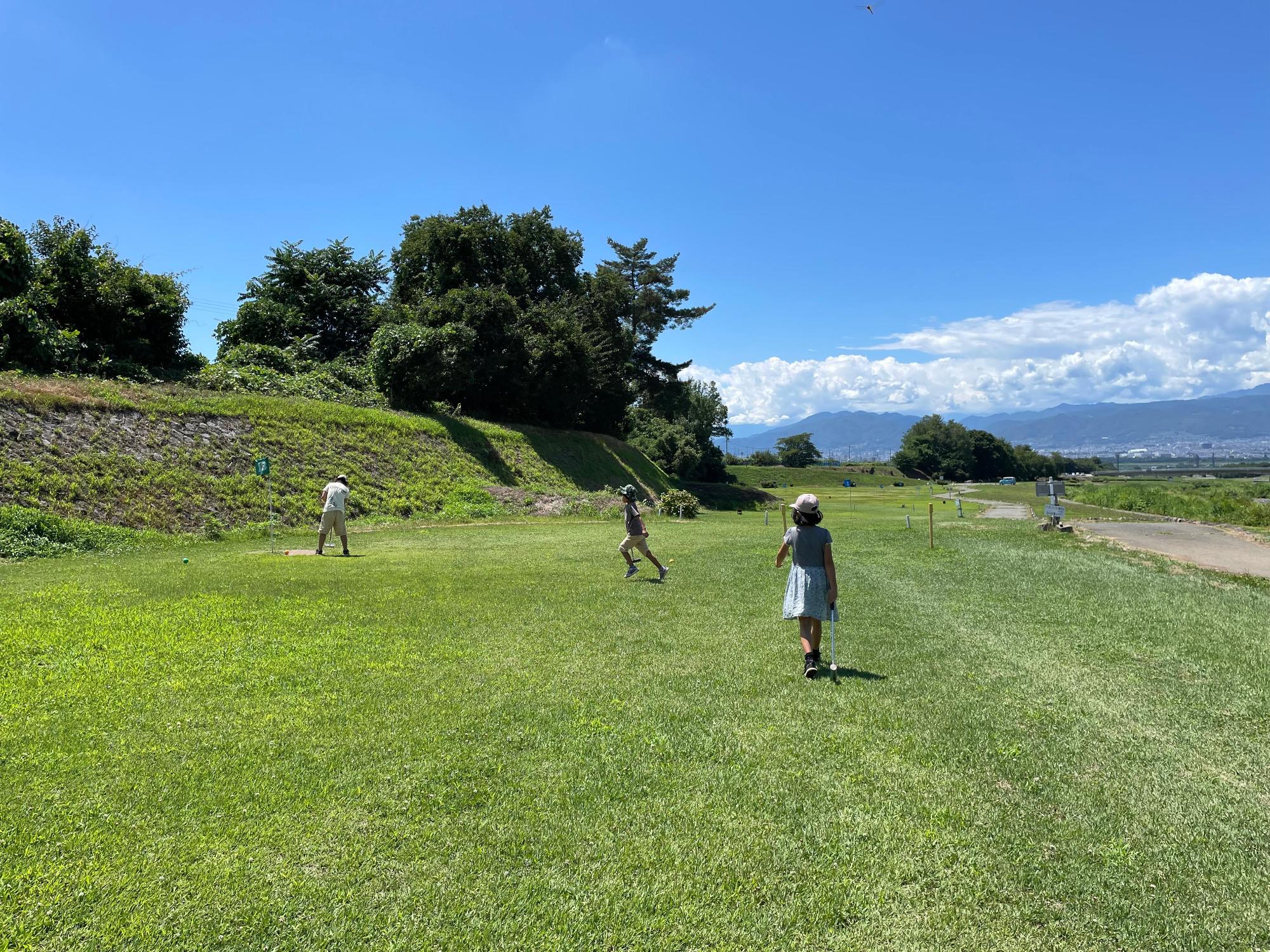 百々川緑地の写真。初夏。芝生が敷き詰められた河川敷で、フリスビーか何かで遊ぶ親子。広くて思いっきり遊べて気持ちよさそう。