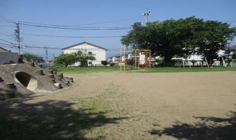 広大な敷地の左手前にトンネルや突起物がある築山があり、その右側奥にブランコなどの遊具がある旭ヶ丘公園の写真