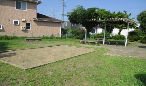 手前に長方形の砂場が設置され、その奥に木陰で休めるベンチがある蒔田公園の写真