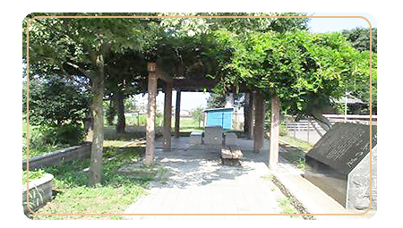 右側に石碑があり中央に草や木が生え、屋根のあるベンチがある塩川上部公園の写真
