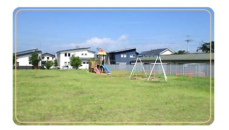 広大な敷地の手前にブランコとその奥に滑り台など複合遊具がある北旭ヶ丘公園の写真