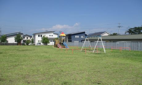 広大な敷地の手前にブランコとその奥に滑り台など複合遊具がある北旭ヶ丘公園の写真