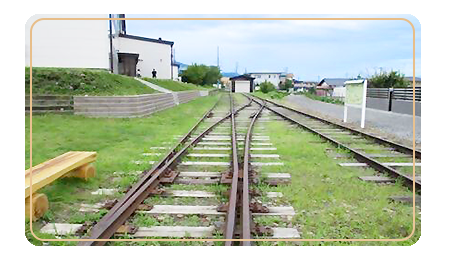 廃線になった長野電鉄河東線の線路が手前から奥へと続く左手前に、木のベンチと奥に進んだ右側に駅標がある河東線記念公園の写真