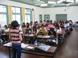 参加した大学生がパイプ椅子に座って女性の話を聴いている写真