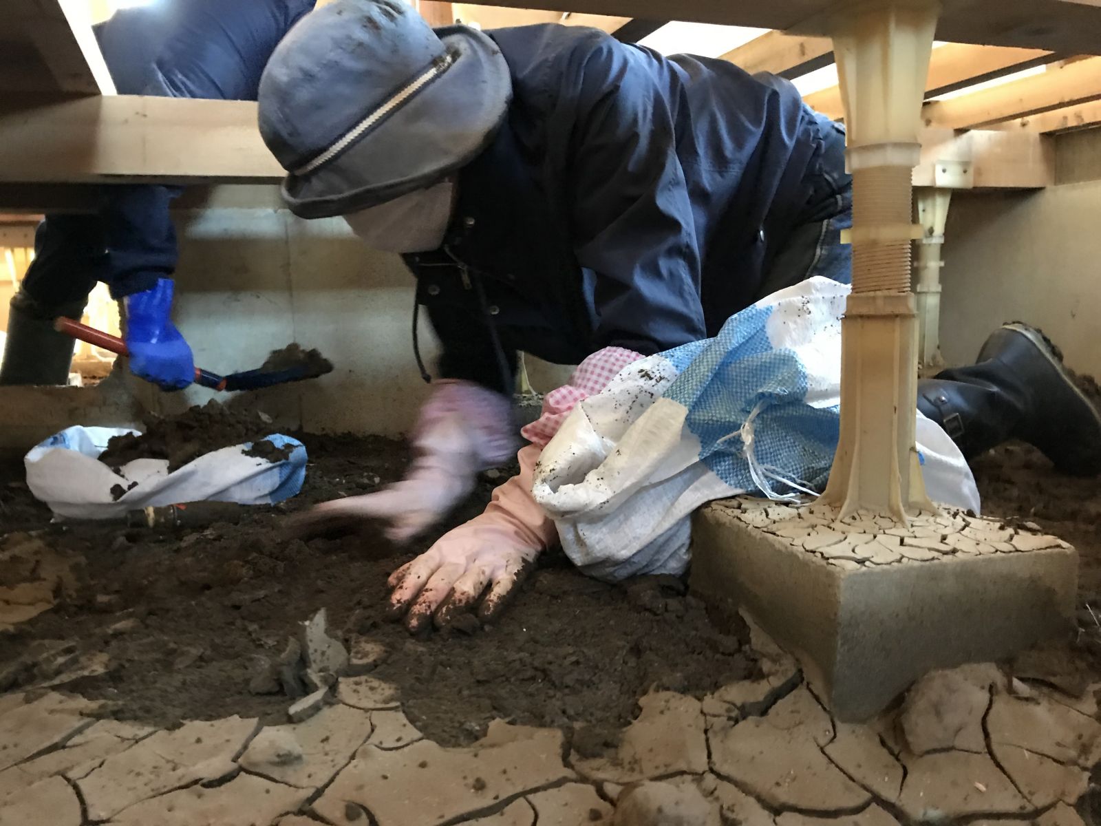ボランティアの人が住宅の床下の泥を撤去している写真