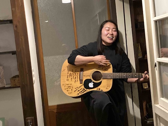 たくさんのメッセージが書かれたギターを弾きながら旅人の歌を歌う堀口直美さんの写真