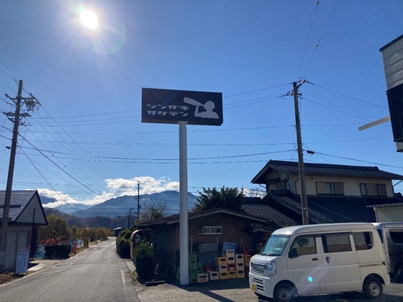 太陽に照らされた黒地に白色でシンザキサケテンの文字とボトルを飲む人がイラストで書かれた長方形黒色の看板の写真
