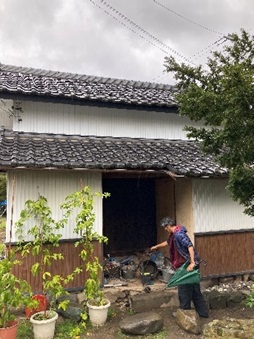 瓦屋根、白を基調とした外壁の土蔵と土蔵入口で緑色の傘を持って改造作業をする若林敦さんの写真