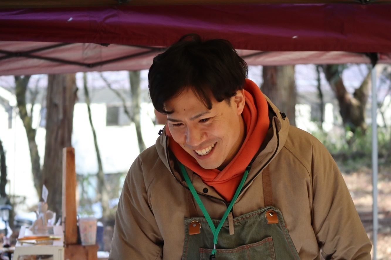 野外にて、はにかみながら下方向を向いている北 直樹さんの写真