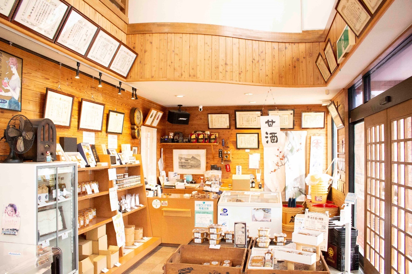 棚や箱、冷蔵庫に商品が並ぶ木を基調とした糀屋本藤醸造舗店内の写真