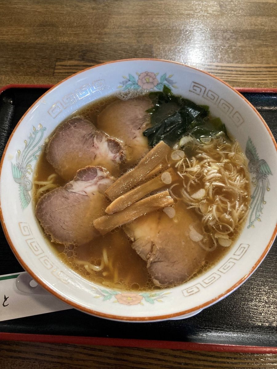 黒いお盆にのったチャーシュー、わかめ、ネギ、メンマがトッピングされたラーメンの写真