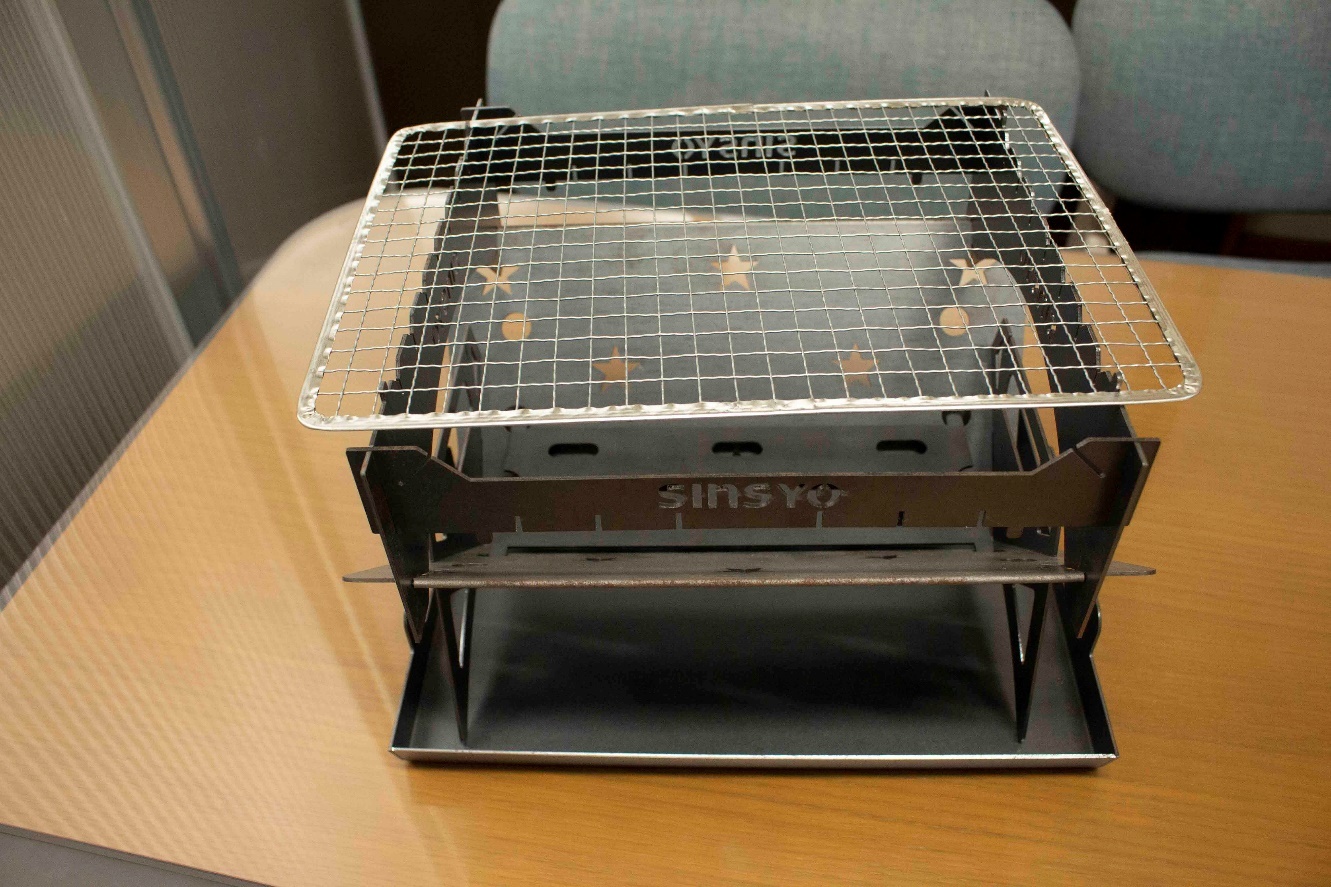 網が乗せられたSINSYOという文字や星、丸などの形が打ち抜き加工された焚火台写真