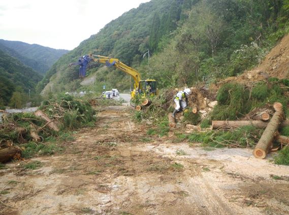 山々を背に黄色のパワーショベルで国道復旧工事作業をする作業員の方の写真