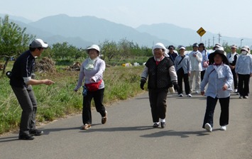 田畑の広がるのどかな風景の道路を参加者の皆さんがウォーキングしている写真