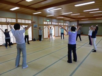 広い和室で参加者たちが大きな円を作り両手を広げて立ちエクササイズ行っている様子の写真