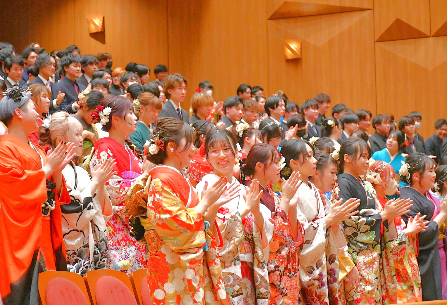 「二十歳を祝う会」で振袖やスーツを着た出席者たちが拍手をしている