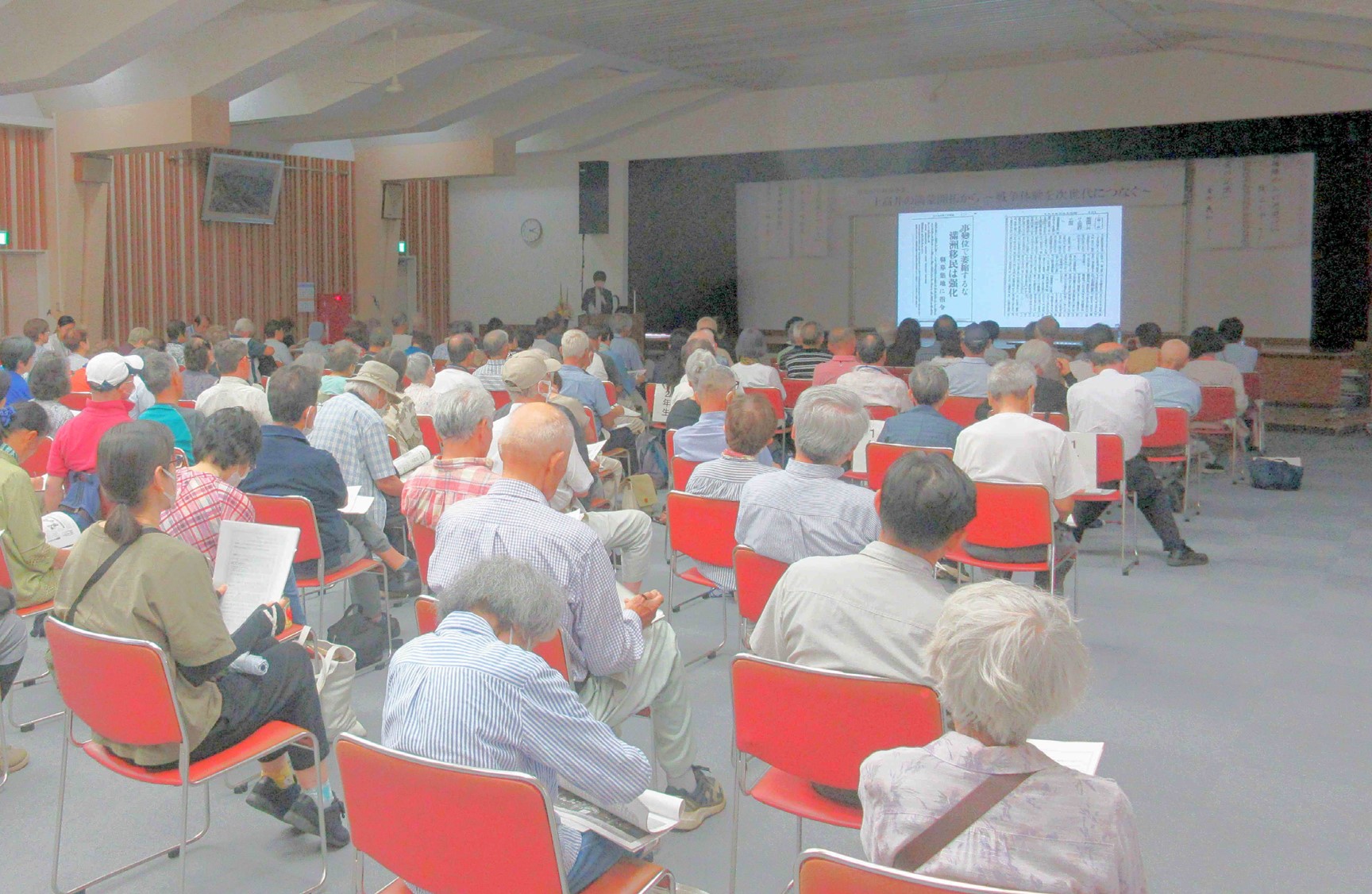 生涯学習センター3階ホールで講演を聞く受講者たち、前面のスクリーンに資料が映し出されている