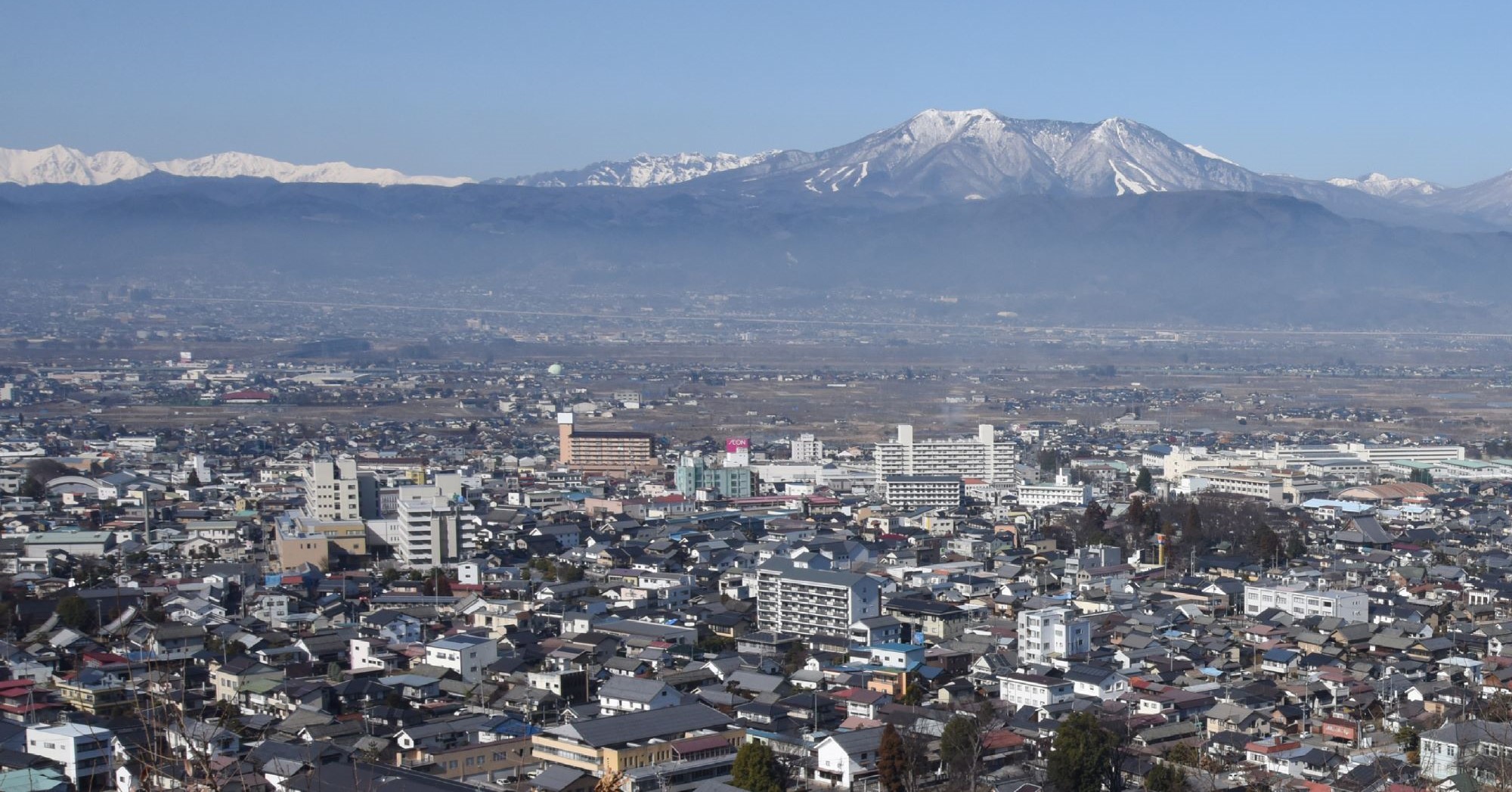 鎌田山山頂から須坂駅方面を中心に人家を撮影した写真。奥に、北アルプス、戸隠連山、飯綱山が写る。
