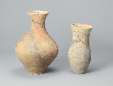 2つの土器が移っている写真。白とベージュの中間のような色の入れ物。ひとつは花瓶のような形で、入り口からくびれがありしたに行くと大きく膨らんでいる。もうひとつは筒状の入れ物。線で模様が描かれている。
