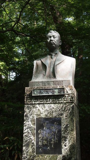 スーツでネクタイをしめ、口ひげをたくわえ、髪の毛は七三になでつけている男性の胸像。