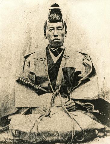 堀なおとらの写真。セピア色のモノクロ写真で、裃を身に着け、刀を差して正座をして正面を向いている。左手には扇のようなものを持っている。