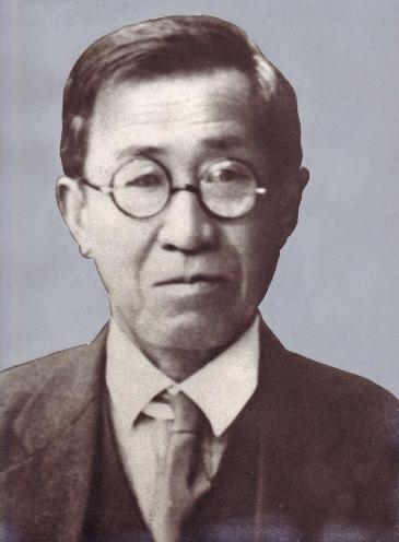 おおば氏の写真。スーツ姿、丸眼鏡をかけた男性。