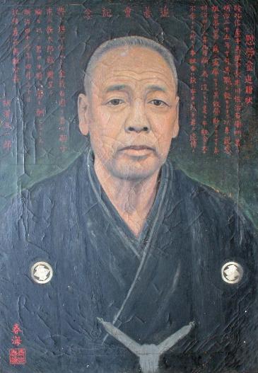 いちかわさじうえもんの肖像画。紋付羽織で頭は白髪の刈り上げ、背景部分には市川氏の功績をたたえる文章が書かれている。