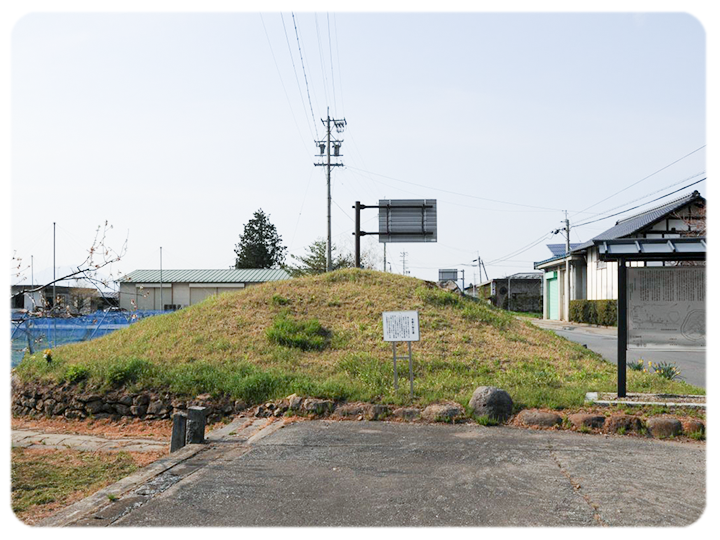 本郷大塚古墳の写真。民家とぶどう畑の中に突如、円錐方の土の盛り上がりがある。