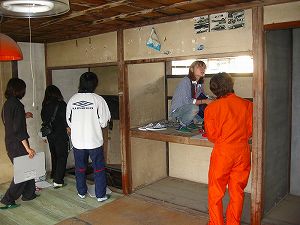 オレンジ色のつなぎを着た男子学生、押入れに上っている女子学生、室内を見て回っている3名の学生たちの写真