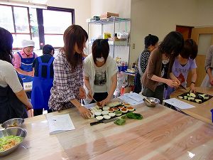 木製のテーブルの上で料理の盛り付けをする大学生たちの写真