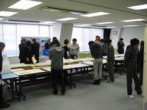 長机の上に並べられた複数の作品を見て回る大学生たちの写真
