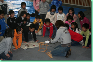 両大学の学生が講師として立体造形を作っているところを小学生が見学している写真