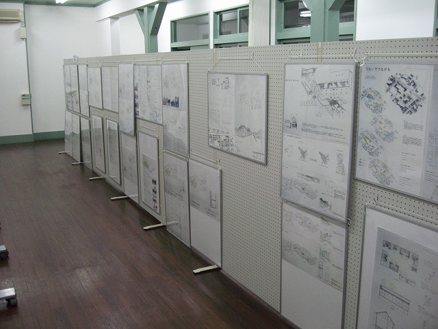 信州大学工学部2年生が作成した「住宅の設計」の作品が、横一列に並べられた展示パネルに設置されている写真